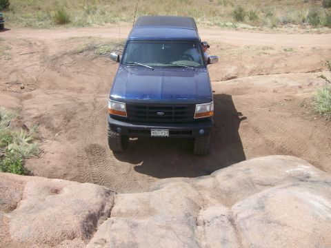 1993 Ford Bronco - A blue Ford Bronco navigates a rocky off-road course on a sunny day.