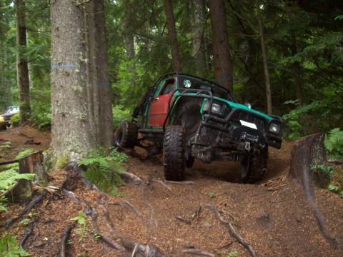 1985 Toyota Pickup/SR5 - A heavily modified truck navigates a wooded trail, with another vehicle visible in the background.
