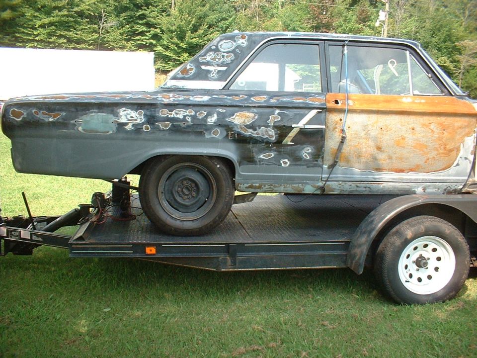 Side view of rusty black project coupe on a flatbed trailer