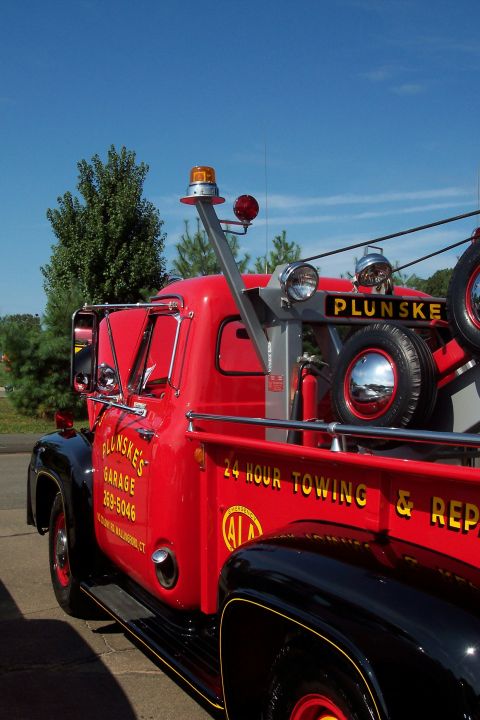 2001 Ford Crown Victoria - A vintage red tow truck with 'Plunskes Garage' and '24 Hour Towing & Repair' lettering is parked under a clear blue sky.