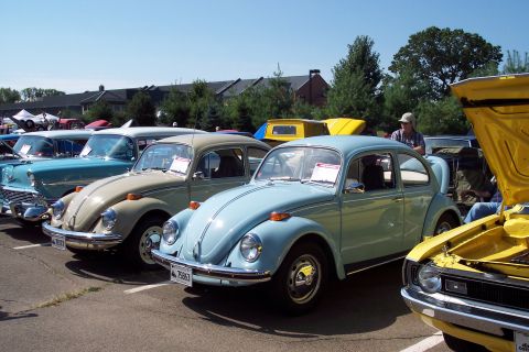2001 Ford Crown Victoria - Several Volkswagen Beetles are lined up at a car show, with a yellow car's hood open in the foreground.
