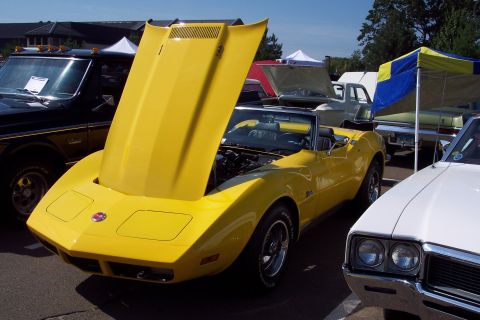 2001 Ford Crown Victoria - A yellow 1975 Corvette convertible is displayed with its hood open at a car show, alongside other vehicles.