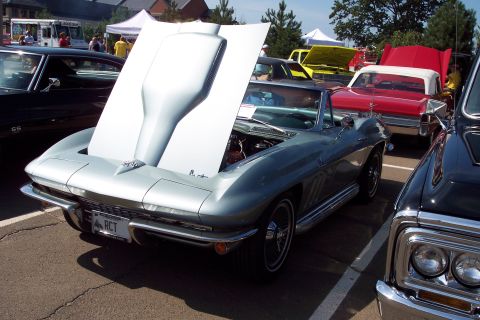 2001 Ford Crown Victoria - A silver 1963 Chevrolet Corvette Sting Ray convertible is displayed with its hood open at a car show, alongside other vehicles.