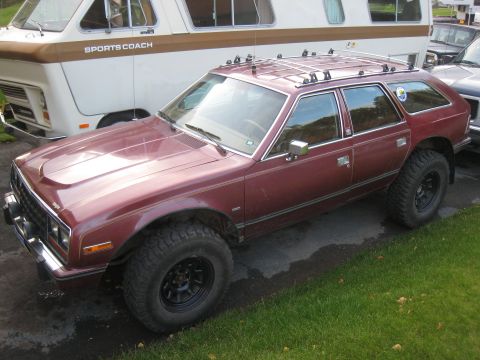 2000 Ford E350 - This lifted station wagon, likely from the early 1980s, features aggressive off-road tires and a roof rack, contrasting with the parked cam…