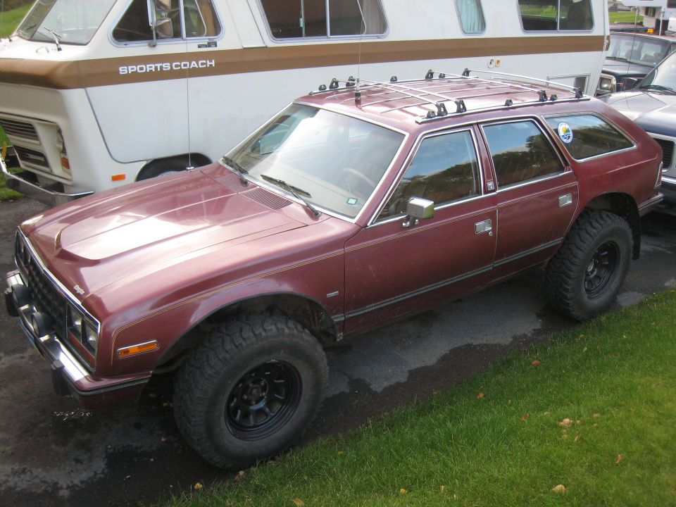 Maroon station wagon with off-road tires and roof rack parked next to a camper van