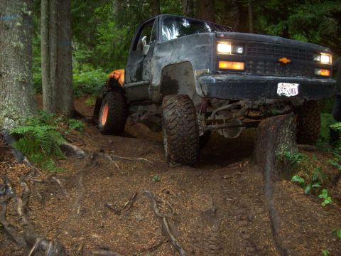 1985 Toyota Pickup/SR5 - This Chevrolet pickup truck is navigating a challenging off-road trail in a wooded area.