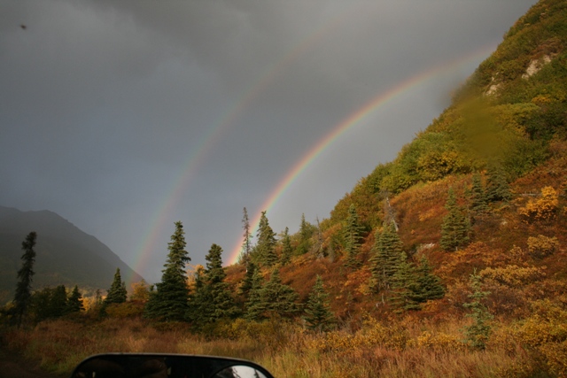 Double rainbow arcs over a forested mountainside with autumn foliage