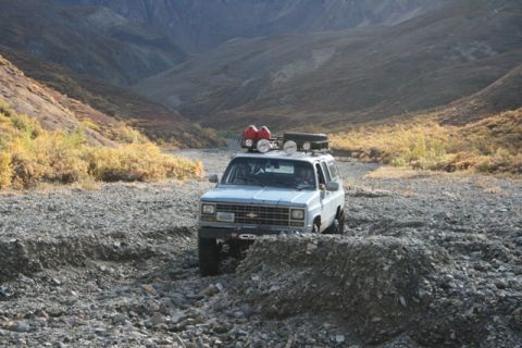 1990 Chevrolet Suburban - An older model SUV navigates a challenging rocky terrain in a mountainous landscape.