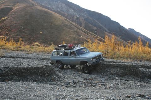 1990 Chevrolet Suburban - An older model SUV navigates a challenging rocky path in a mountainous, autumnal landscape.