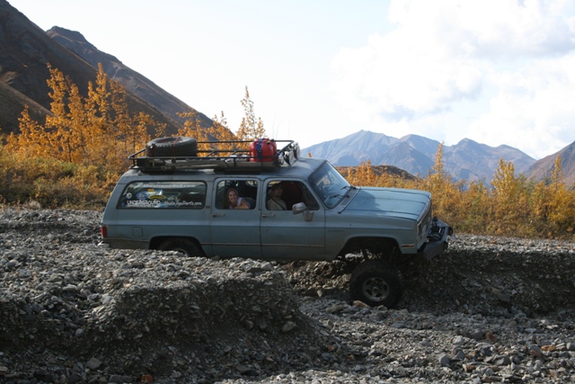 1990 Chevrolet Suburban driving over rocky terrain with mountains in background