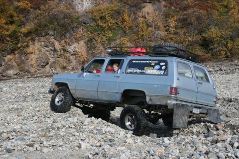 1990 Chevrolet Suburban - Chevrolet Suburban tackles rough terrain with off-road modifications and occupants.