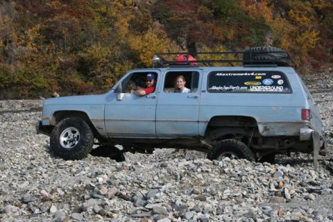1990 Chevrolet Suburban - Two people are inside a light blue SUV navigating a rocky, off-road environment.