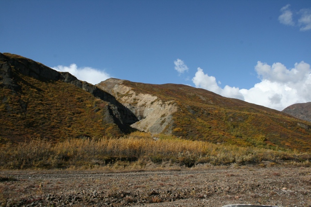 Mountain slopes covered in autumn brush under a blue sky with scattered clouds