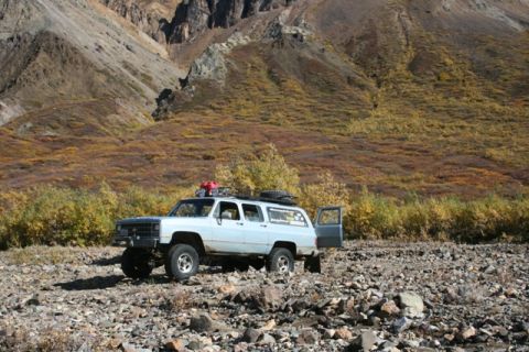 1990 Chevrolet Suburban - An older model SUV sits in a rocky landscape with mountains and fall colors behind it.