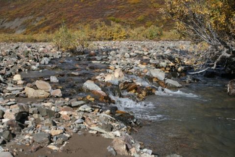 1990 Chevrolet Suburban - A natural scene of a stream flowing through a rocky bed, with hills covered in autumn foliage in the background.