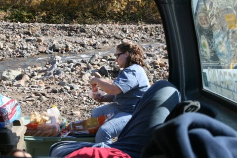 1990 Chevrolet Suburban - A woman eats from a container while sitting inside a vehicle parked near a stream.