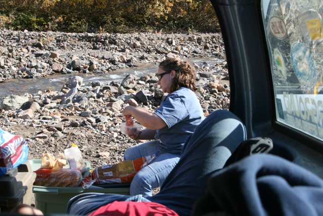 Interior view of a vehicle with a woman eating by a rocky stream outside