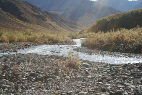 1990 Chevrolet Suburban - A wide mountain valley features a winding river flowing through a rocky terrain under a clear sky.