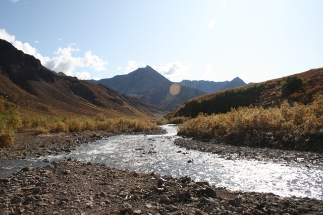 Mountain valley with a river flowing through it. Mountains and brush are visible