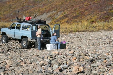 1990 Chevrolet Suburban - A light blue 1990 Chevrolet Suburban is parked on a rocky surface, with two people standing near the open rear doors.