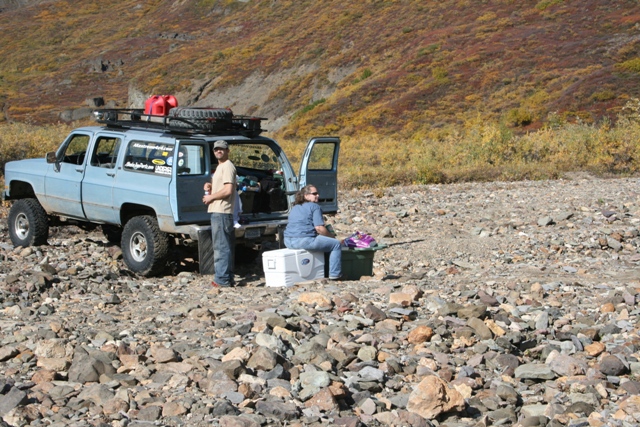 Light blue 1990 Chevrolet Suburban with roof rack and spare tire parked on rocky terrain