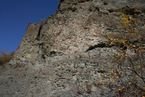 1990 Chevrolet Suburban - A rocky cliff face under a bright blue sky, with autumn foliage visible on the right side.