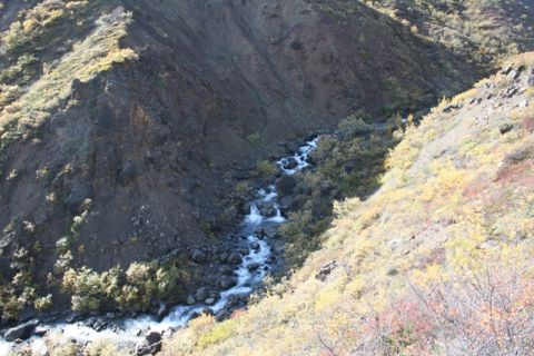 1990 Chevrolet Suburban - A fast-flowing stream cuts through a , rocky landscape dotted with trees displaying fall colors.