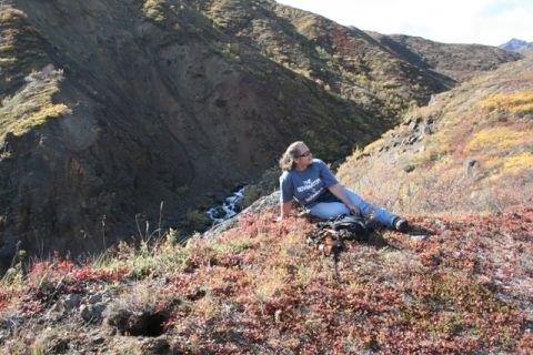 1990 Chevrolet Suburban - A woman rests on a hillside covered in autumn foliage, with a stream flowing through the valley below.