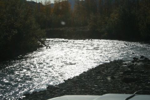 1990 Chevrolet Suburban - A river flows over rocks with trees on the bank under a bright sun.