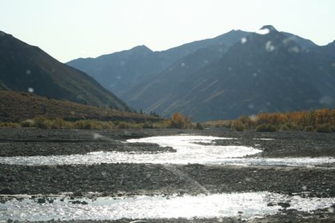 1990 Chevrolet Suburban - A wide, rocky riverbed with shallow water reflecting the sunlight, set against a backdrop of mountains.