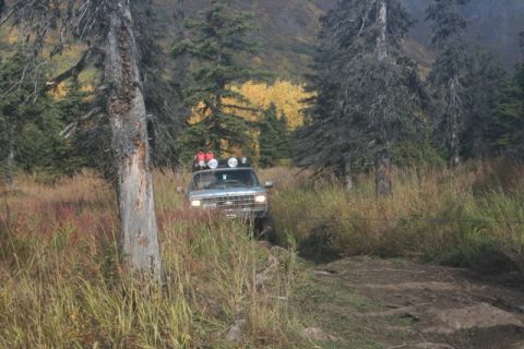1990 Chevrolet Suburban - A silver Chevrolet Suburban navigates a wooded trail with autumn foliage in the background.