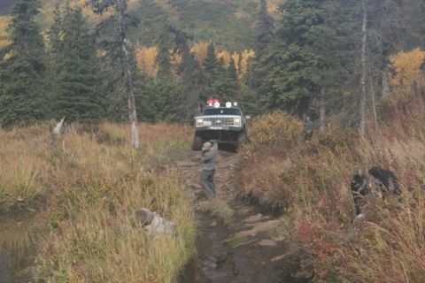 1990 Chevrolet Suburban - A 1990 Chevrolet Suburban navigates a challenging, muddy off-road trail surrounded by autumn foliage.