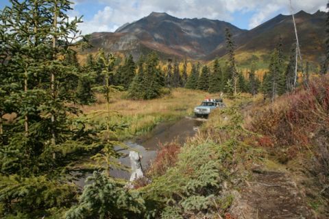 1990 Chevrolet Suburban - An SUV navigates a water crossing on a remote mountain trail during autumn.