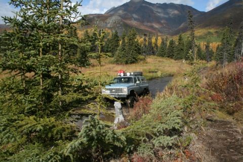1990 Chevrolet Suburban - A light blue 1990 Chevrolet Suburban navigates a watery path amidst autumn foliage and mountains.