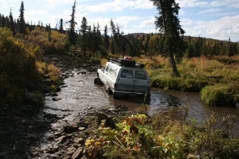 1990 Chevrolet Suburban - A gray 1990 Chevrolet Suburban navigates a muddy stream on an off-road trail.