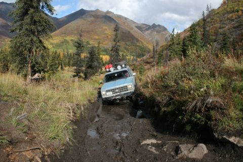 1990 Chevrolet Suburban - An off-road vehicle tackles a challenging muddy path in a mountainous, wooded area during autumn.
