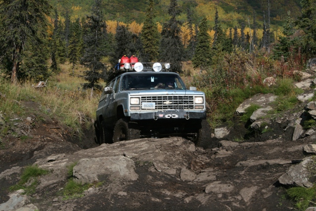 Silver SUV with roof rack, off-roading on a rocky, muddy trail