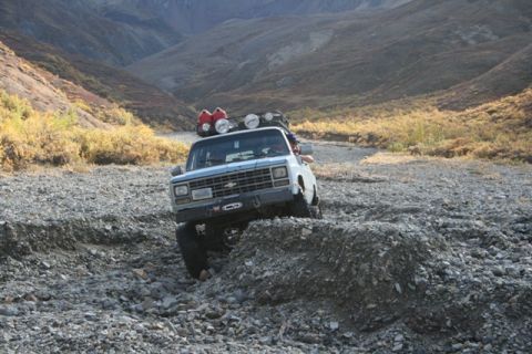 1990 Chevrolet Suburban - A lifted pickup truck navigates a rocky terrain, suggesting an off-road adventure in a mountainous area.