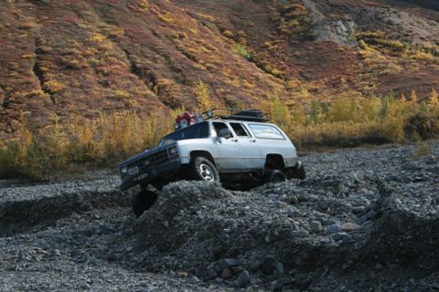 1990 Chevrolet Suburban - An older model SUV navigates a rocky, off-road terrain with autumn foliage on the hillside.
