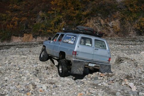 1990 Chevrolet Suburban - This 1990 Chevrolet Suburban is navigating a challenging rocky trail with autumn foliage in the background.