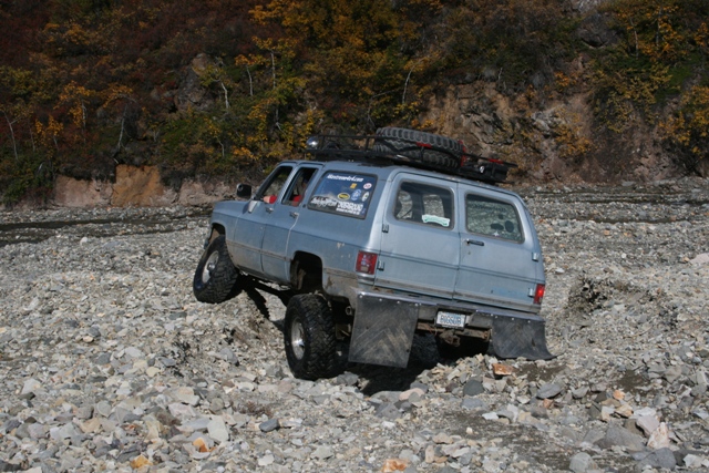1990 Chevrolet Suburban with lifted suspension and off-road tires driving over rocks