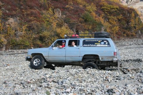 1990 Chevrolet Suburban - A light blue Chevrolet Suburban navigates a rocky terrain with fall foliage in the background.