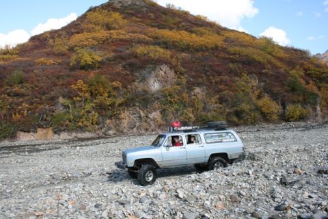 1990 Chevrolet Suburban - A 1990 Chevrolet Suburban navigates a rocky riverbed under a colorful mountain landscape.