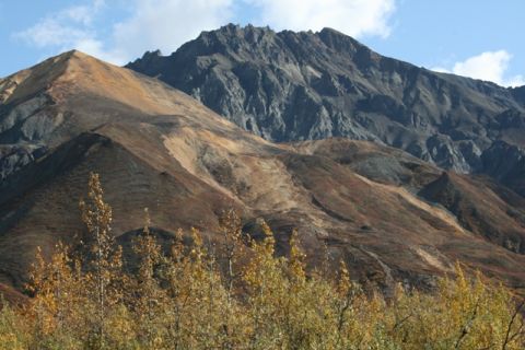 1990 Chevrolet Suburban - A vast mountain range under a blue sky with scattered clouds, slopes in shades of brown and grey, with yellow and orange foliage in the for…