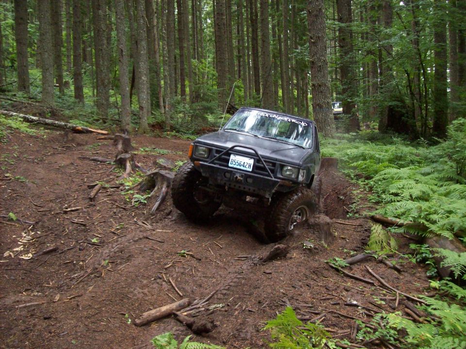 Black off-road truck with large tires navigating a muddy, wooded trail