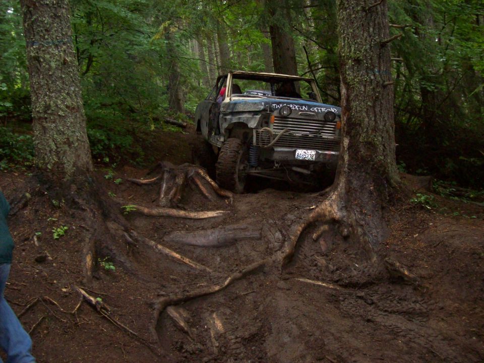 Muddy off-road truck climbing over tree roots on a steep forest trail