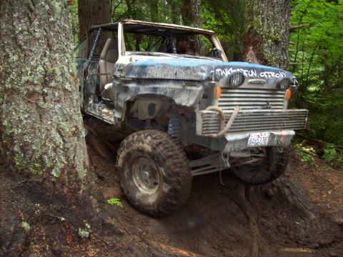 1985 Toyota Pickup/SR5 - Custom off-road truck tackling a challenging muddy trail in a forest setting.