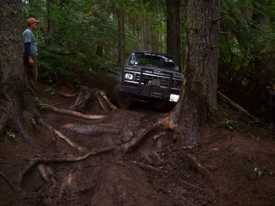 Black off-road vehicle navigating a steep, muddy, root-covered trail in a forest