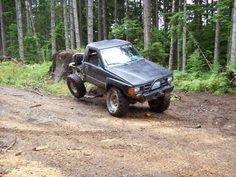 1985 Toyota Pickup/SR5 - This lifted 1985 Toyota Pickup/SR5 navigates a muddy trail through a dense forest.