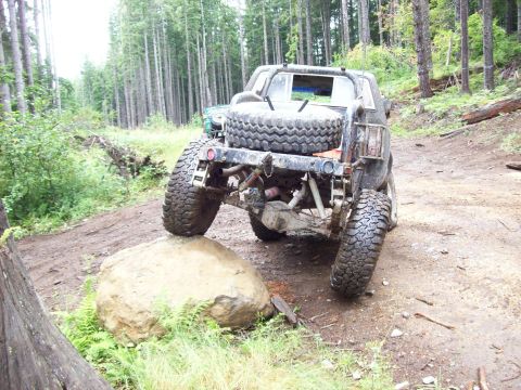 1985 Toyota Pickup/SR5 - Off-road pickup truck navigating a large rock on a trail, with another vehicle visible in the background.